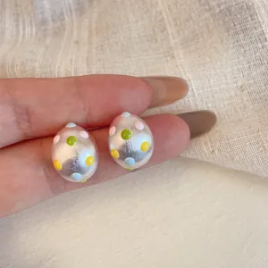Dettaglio di orecchini a lobo ovali argento opaco con pois colorati dipinti a mano.