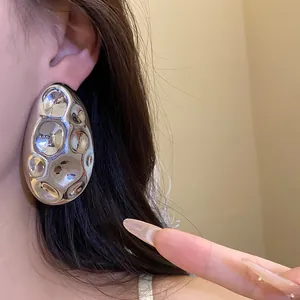 Macro detail of a large silver oval metal stud earring featuring a unique hammered texture