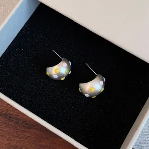Primo piano di orecchini minimalisti in argento opaco a forma di C con pois colorati in scatola.