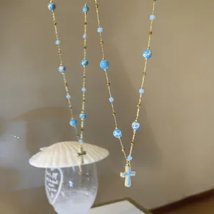 Detail shot of a vintage blue beaded necklace with a gold-rimmed cross pendant.
