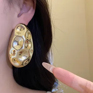 Close-up of elegant gold oval hammered stud earrings with vintage texture worn on ear
