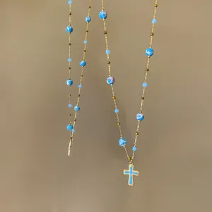 Close-up of a vintage-style beaded necklace featuring a blue enamel cross pendant.