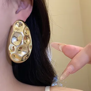 Detailed macro view showing the hammered metallic texture of gold oval earrings worn on an ear