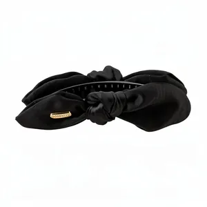 Barrette banane élégante en satin noir noué avec un détail de logo doré décoratif
