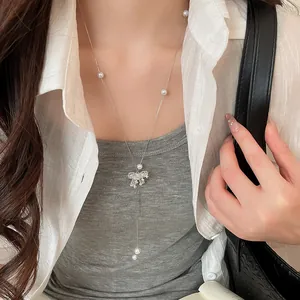 Macro view of a sparkling bow Y-shape pearl necklace worn with an elegant white shirt