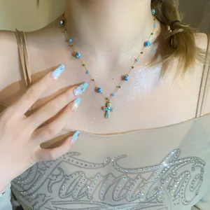 Detailed view of a vintage blue enameled cross necklace with stone beads on model
