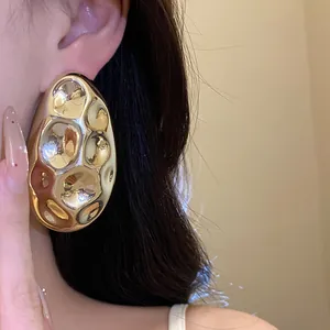 Close-up of vintage metallic oval stud earrings with hammered texture in golden finish