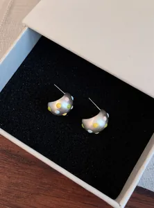 Dettaglio di orecchini a lobo a forma di C in argento opaco con pois in smalto colorati