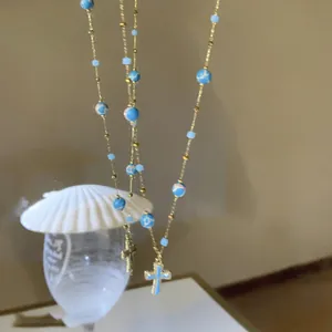 Detailed view of blue beaded necklace with enamel cross pendant in vintage gold finish
