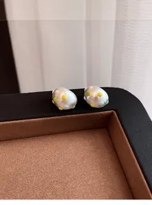 Dettaglio di orecchini a perno ovali argento opaco con pois colorati su vassoio gioielli