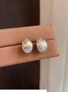 Dettaglio di orecchini a perno ovali a forma di C in argento opaco con pois colorati