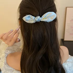 Vue détaillée d'une pince banane en satin bleu clair nouée sur cheveux bruns ondulés