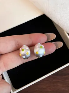 Primo piano di orecchini a lobo ovali in argento opaco con dettaglio smalto a pois.