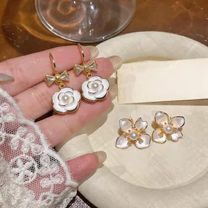 Detailed close-up of elegant camellia flower earrings with pearls and gold bow accents