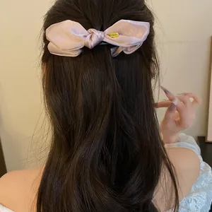 Gros plan montrant la texture élégante d'une pince banane à nœud en satin rose sur cheveux.