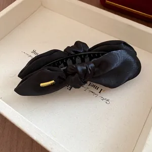 Gros plan d'une pince banane en satin noir noué avec texture élégante et détail doré
