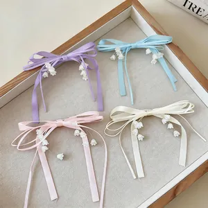 Quattro eleganti fermagli a fiocco con nappe di mughetto presentati in un vassoio di legno