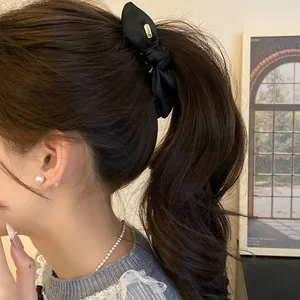 Gros plan d'une pince à cheveux banane en satin noir noué sur une queue de cheval.