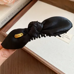 Gros plan d'une pince banane en satin noir noué avec une étiquette dorée rétro.