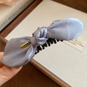 Détail d'une pince à cheveux banane en satin bleu noué avec étiquette dorée