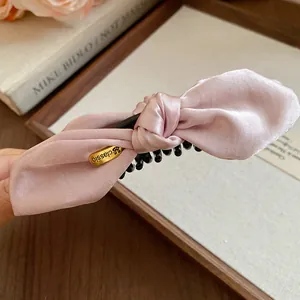 Détail d'une pince banane en satin rose nouée avec texture de tissu et étiquette dorée
