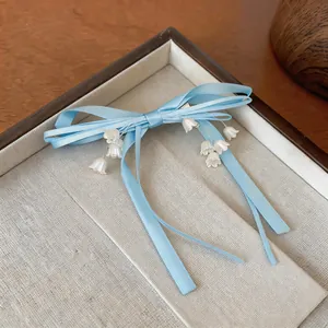 Primo piano di un fermaglio per capelli a fiocco blu con ciondoli a fiore di mughetto