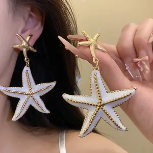 Detailed macro view of oversized white enamel starfish drop earrings with golden metal accents.