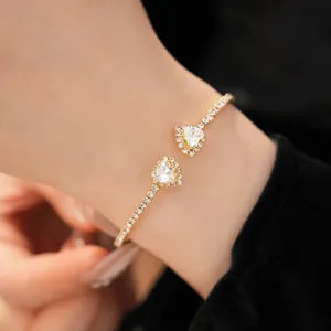 Detail view of a gold open cuff bracelet with sparkling heart-shaped crystal settings