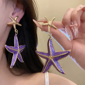 Close-up of purple starfish dangle earrings with gold-toned textured detailing for vacation.