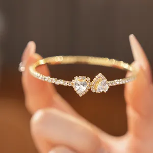 Close-up view of a gold-colored rhinestone bangle featuring two sparkling heart crystals