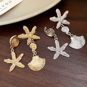 Elegant gold and silver starfish and shell drop earrings on a dark wood background.
