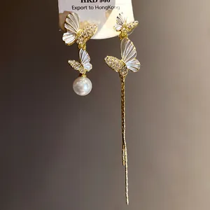 Detalle macro de pendientes de mariposa asimétricos con esmalte blanco y perla