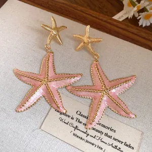Detailed macro view of pink enamel starfish pendant earrings with gold-tone borders.