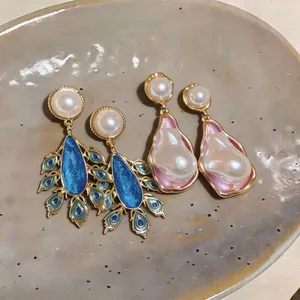 Detailed macro view of vintage irregular pearl earrings with blue peacock and pink shell motifs