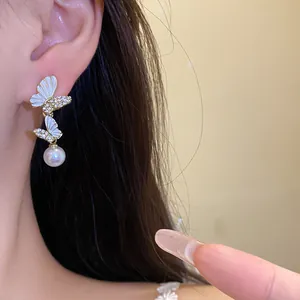 Elegantes pendientes de mariposa con gotas de perlas mostrados en la oreja del modelo.