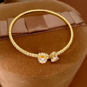 Close-up of gold open bangle with sparkling heart-shaped crystals and pave stones.