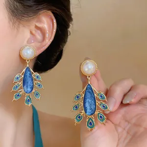Elegant close-up of vintage peacock earrings featuring blue enamel and white pearls.