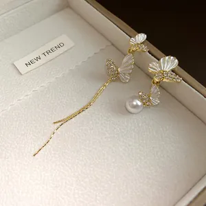 Detalle de pendientes de mariposa asimétricos con perlas y borlas en caja de regalo
