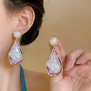 Close-up of irregular pearl drop earrings with elegant gold and purple enamel details.