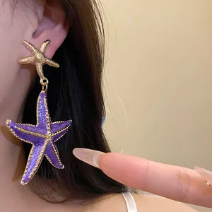 Detailed macro view of elegant purple and gold starfish dangle earrings worn on ear