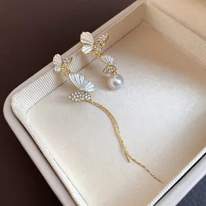 Elegantes pendientes asimétricos dorados con mariposas de cristal y una gota de perla.