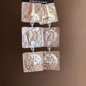 Detailed view of silver square earrings with unique anatomical ear and nose embossed motifs