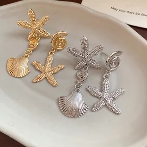 Close-up of gold and silver starfish and shell drop earrings on a ceramic tray