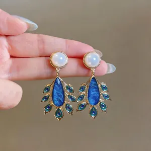Exquisite detail of palace style peacock feather enamel earrings featuring pearls in gold finish