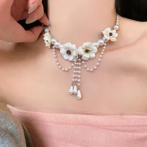Primo piano di una collana in stile francese con fiori bianchi e nappe di perle.
