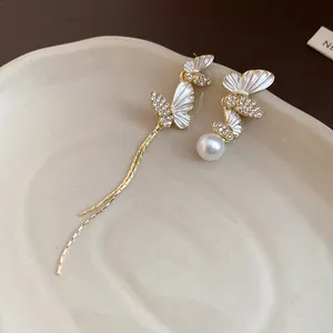Detalle de elegantes pendientes de mariposa dorados con esmalte, pedrería y perlas.