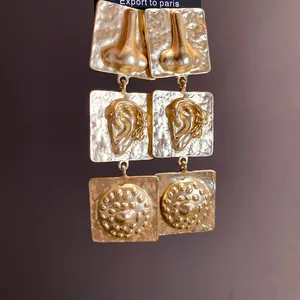 Macro view of gold vintage square earrings with unique ear and nose motifs.