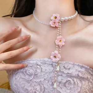 Primo piano di girocollo in perle con fiori di stoffa rosa e perle a goccia pendenti.