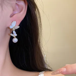 Primer plano de los elegantes pendientes de mariposa con esmalte blanco y gota de perla