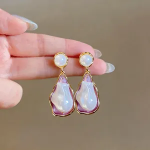 Close-up of elegant irregular pearl drop earrings with purple enamel and gold finish